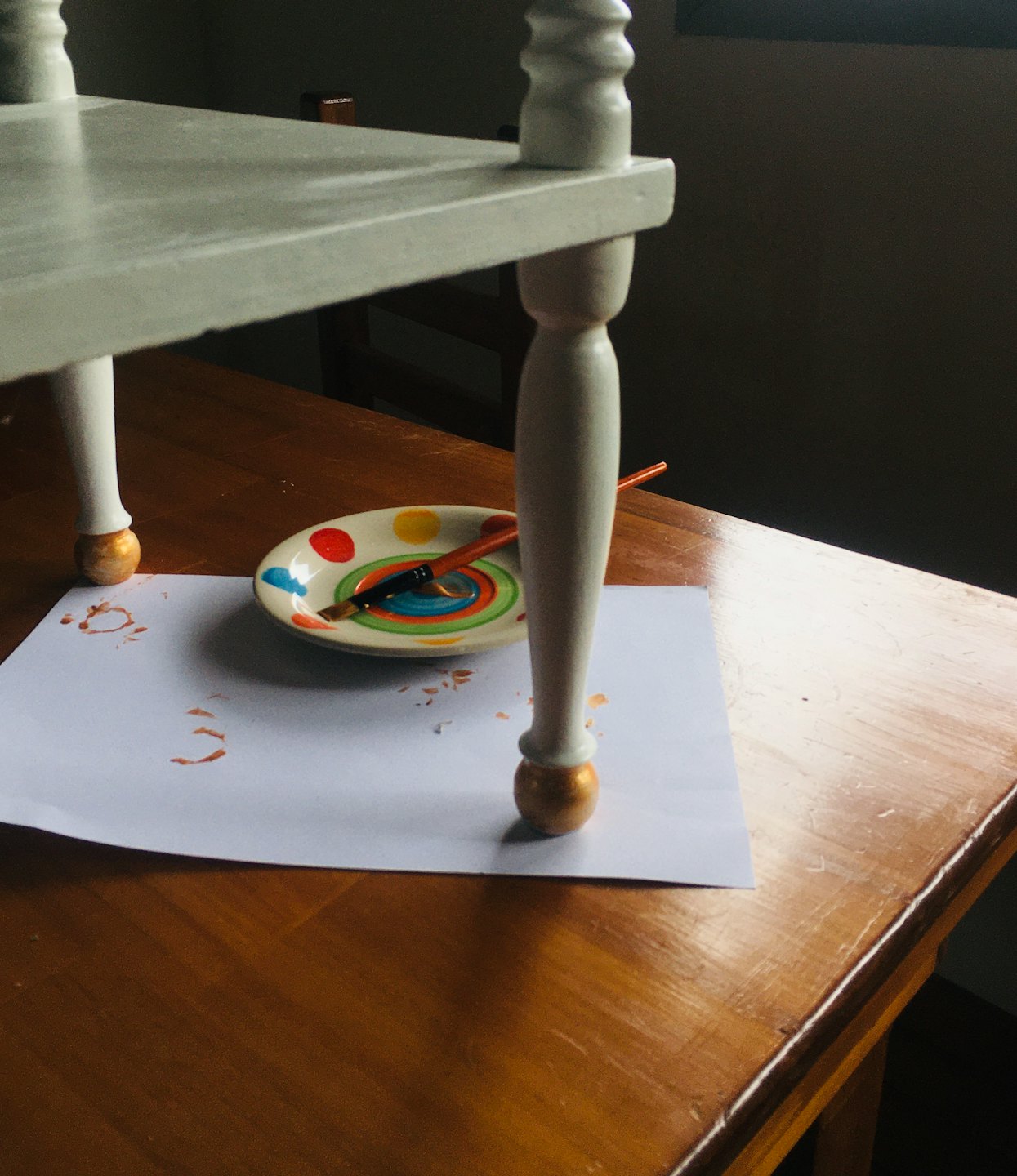 Kunstenaar schildert witte meubelpoot op een houten tafel.