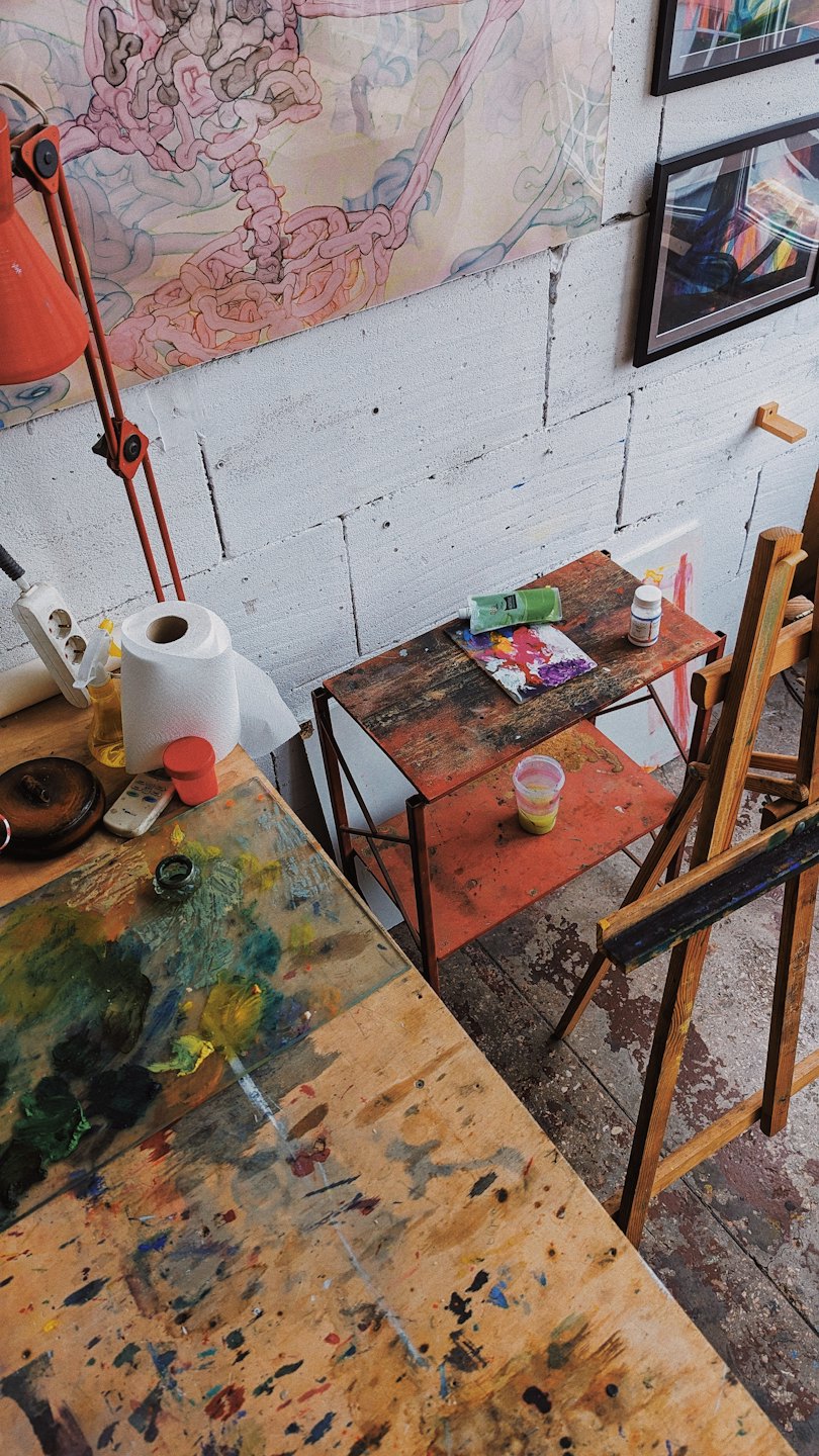 Kunstenaarswerkplaats met verfbenodigdheden en abstracte kunst aan de muren.