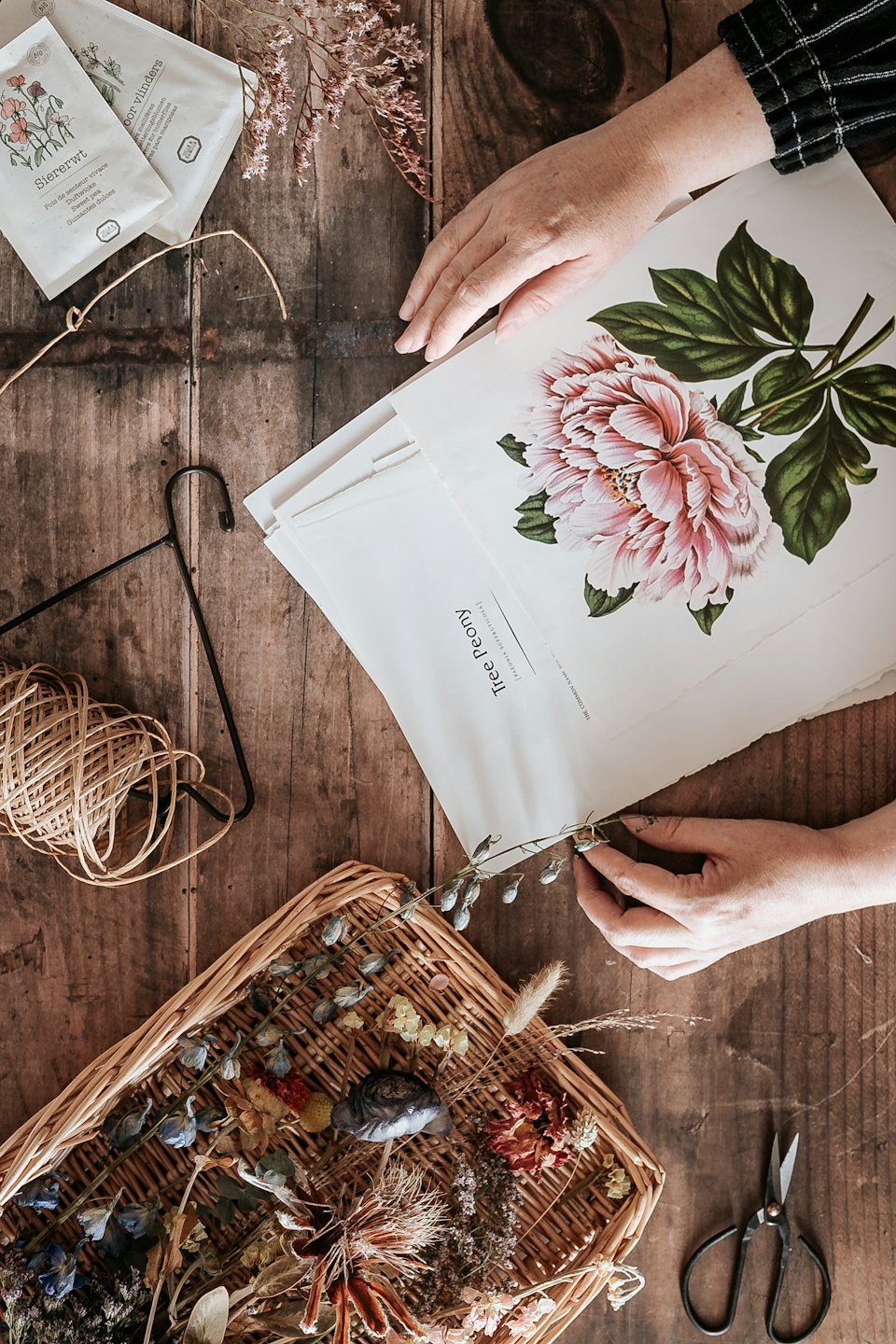 Handen schikken gedroogde bloemen en zaaddozen op een houten tafel.