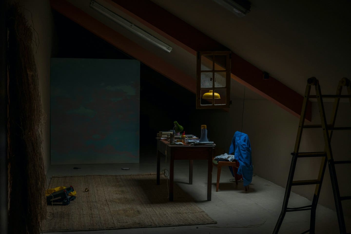 Zolderstudio met schilderij, bureau en ladders.
