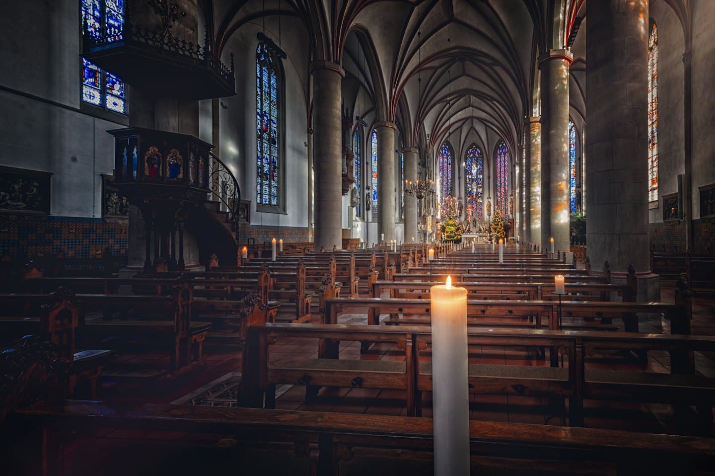 Lege kerkbanken in een gotische kerk met kerstbomen en kaarsen.