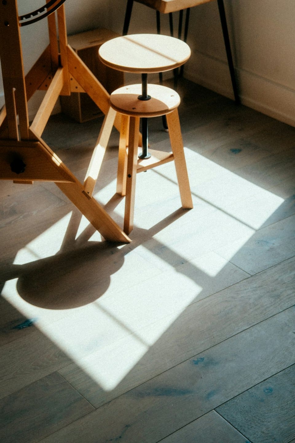 Verstelbaar houten kunstenaarsstoeltje dat schaduwen werpt in een lichte studio.