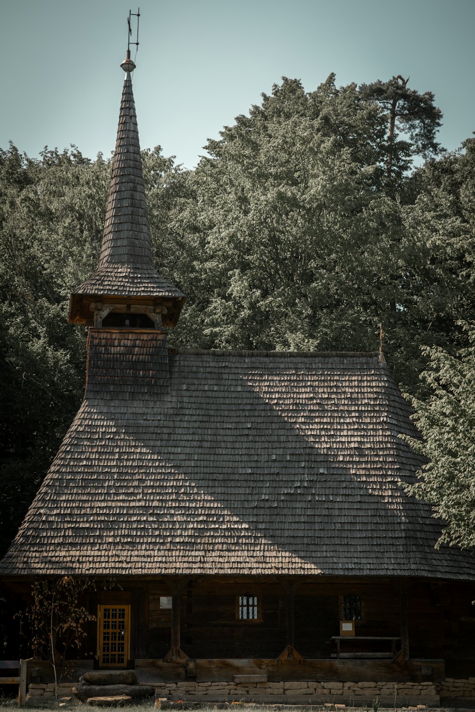 Historische houten kerk met een hoge spits tussen groene bomen.